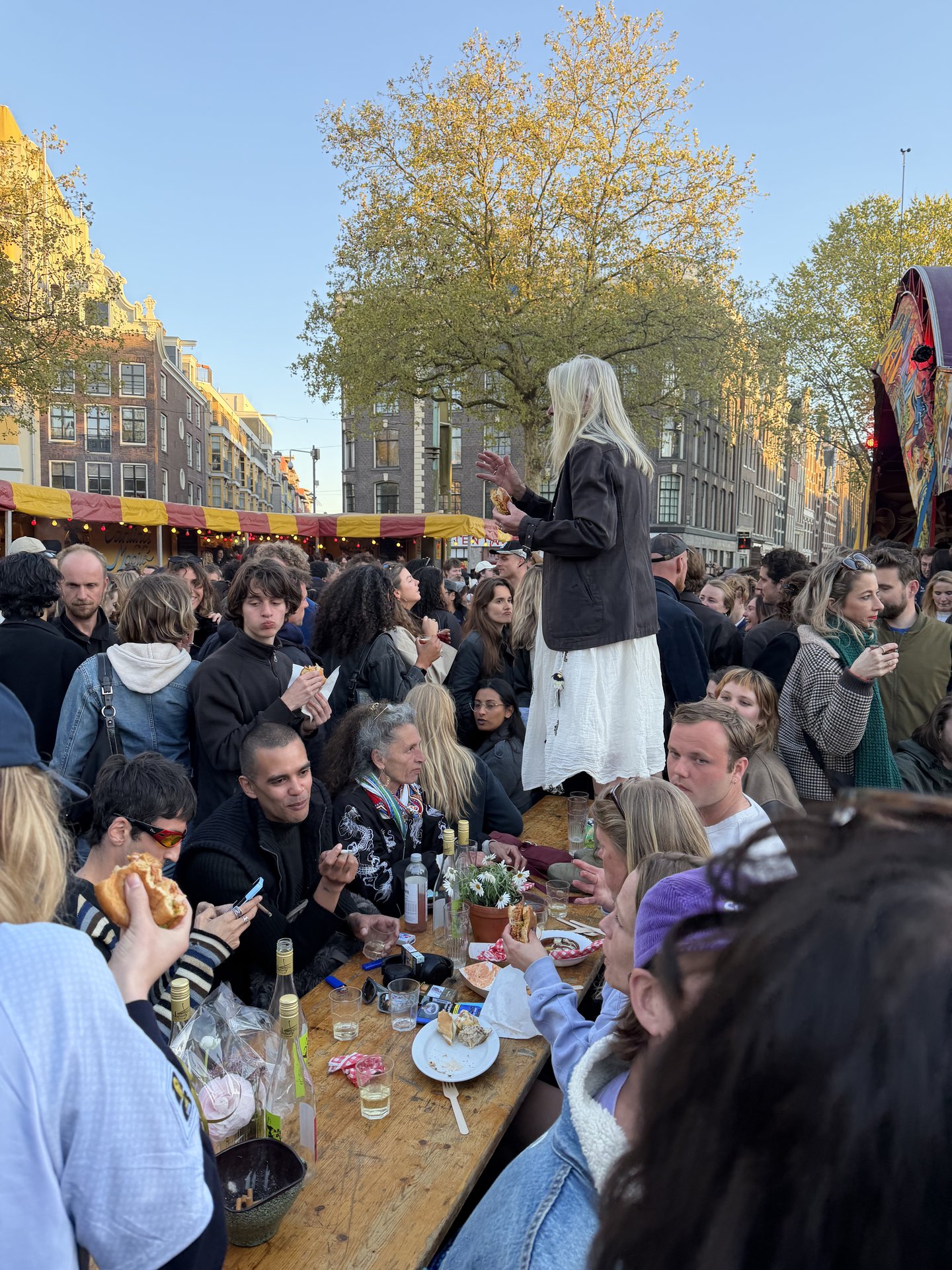 This vibrant photo captures a bustling street festival in Chinatown, Amsterdam, with a large crowd gathered around long wooden tables